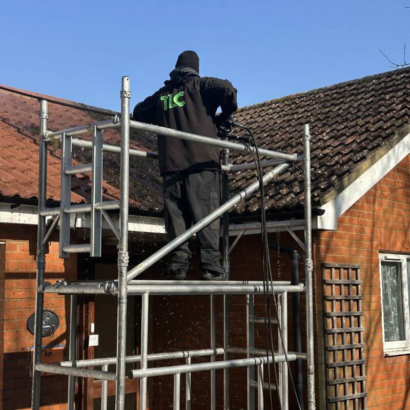 TLC roof cleaning specialist working from scaffolding beside a tiled residential roof.